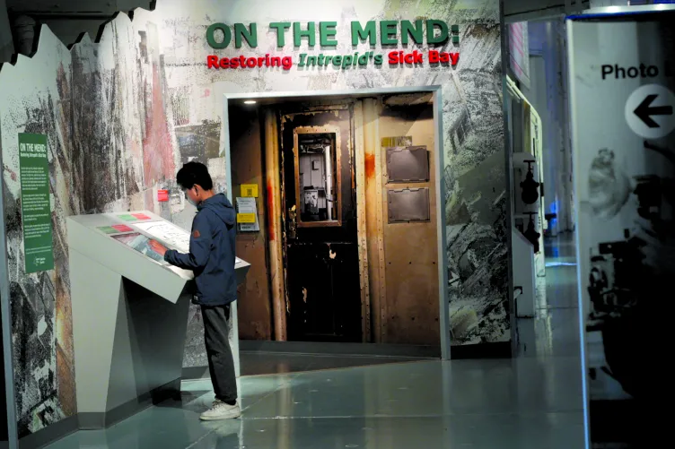 A visitor reads a panel in front of the exhibition "On the Mend: Restoring Intrepid's Sick Bay."